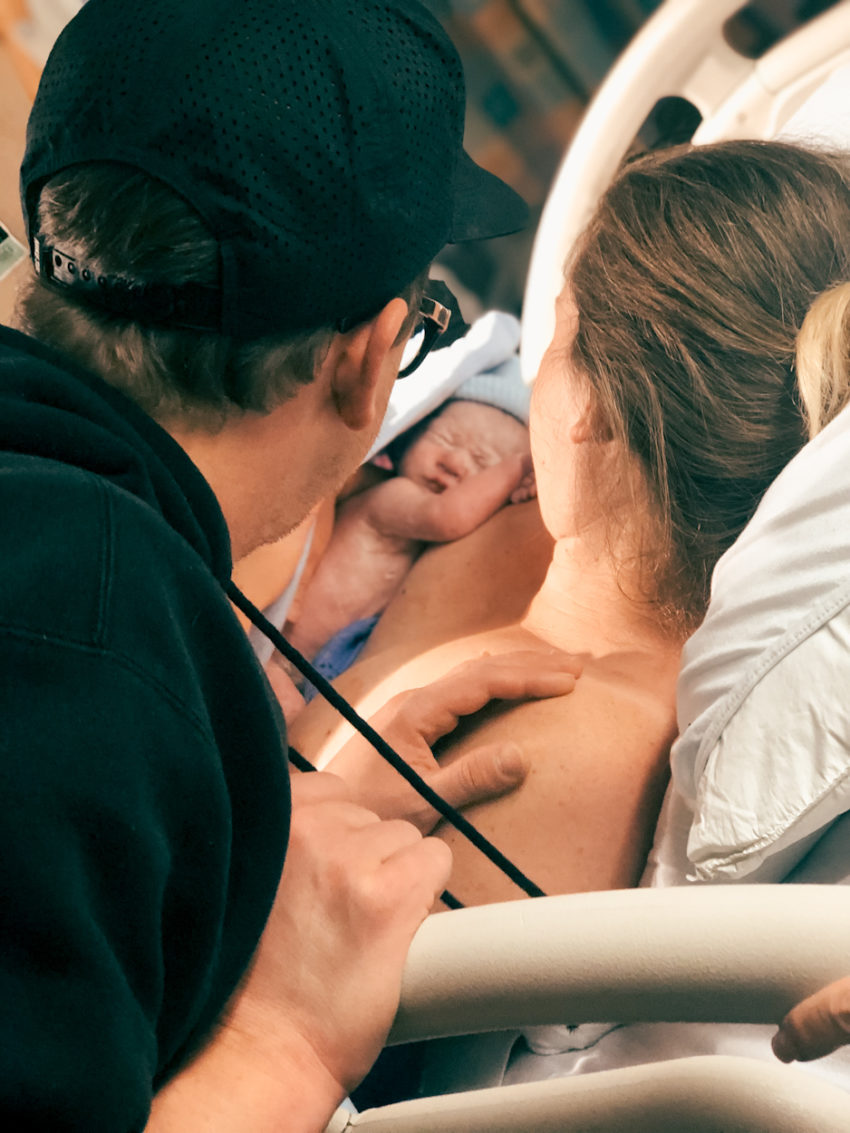 newborn baby on moms chest as dad looks from shoulder