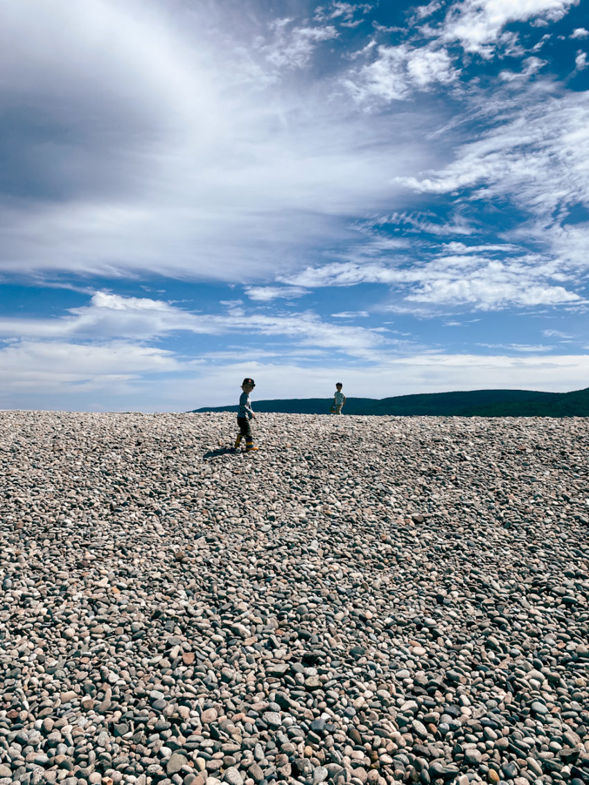 two boys disappearing on the horizon of a rocky beach in the summer along the cape breton trail