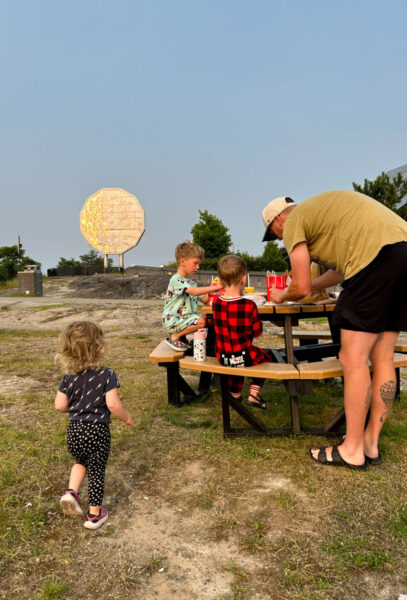 kids sit at a picnic table in fromt of the giant nickel in sudbury, ontario