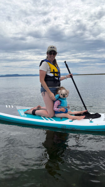 a mom and her 2 year old on a paddle board in the ocean